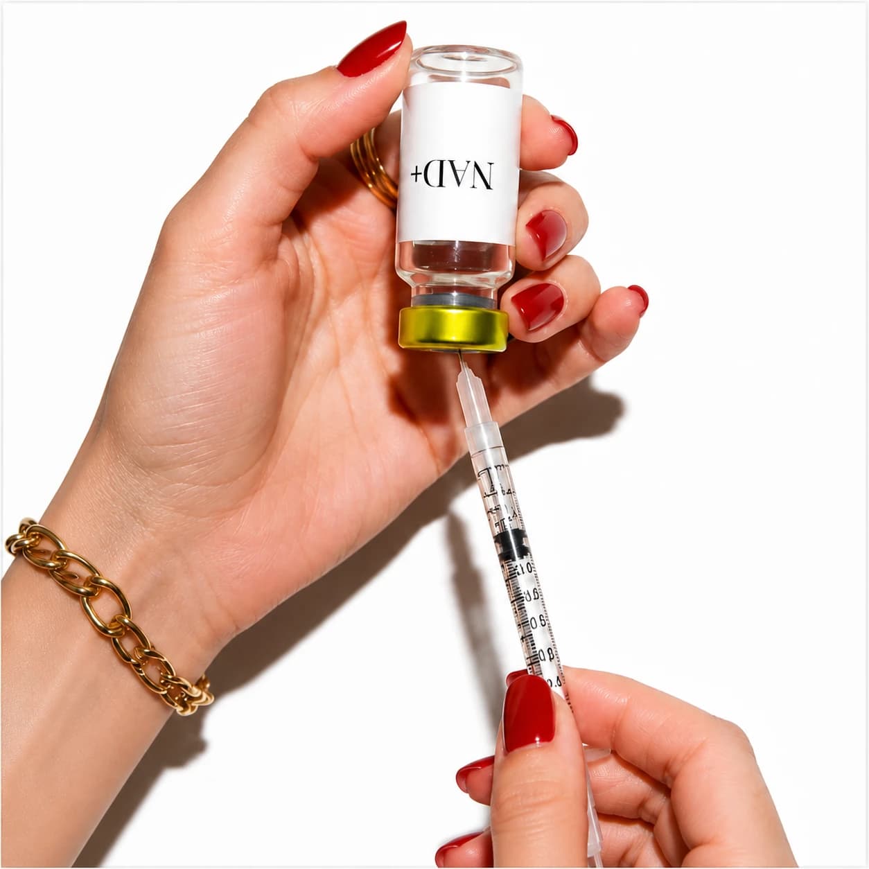 Red-manicured hands with a gold chain bracelet holding a gold-capped NAD+ vial and drawing it into a syringe on a bright white background.